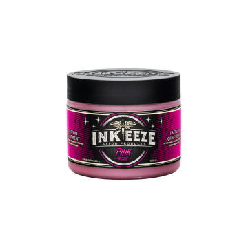 Un pot d'INK-EEZE Pink Glide - Baume pour tatouage multi-usage avec un couvercle noir et une étiquette rose, noire et verte représentant des ailes et des étoiles, sur fond blanc.
