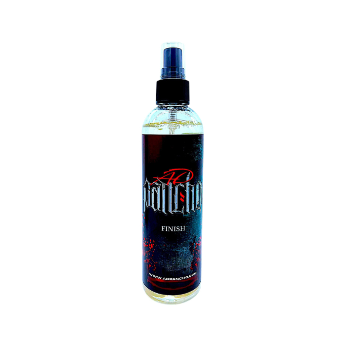 Un flacon pulvérisateur transparent étiqueté « AD Pancho Tattoo Finish 250 ml », avec un motif noir et rouge, présenté sur fond blanc. L’étiquette comporte l’URL d’un site web en bas.